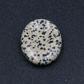Piedra Gua Sha ovalada de jaspe dalmata con textura de manchas negras sobre fondo oscuro - Piedra Manchada