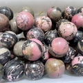 Polished natural pink rhodonite stone spheres with black veins in bulk heap - Red Network Stone