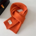Close-up of bright orange knitted scarf texture with rib edging and emo woven label - 20x156cm / Orange