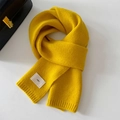 Detailed view of ginger yellow knitted scarf with stylish emo label on smooth surface - 20x156cm / Yellow