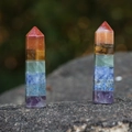 Handcrafted hexagonal seven chakra natural crystal pillars set on a grey rock surface - Rainbow