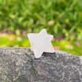 Polished natural rose quartz Merkaba star stone ornament placed on a grey rock surface - Rose Quartz