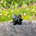 Polished black obsidian Merkaba star crystal stone displayed on a natural rock surface - Obsidian