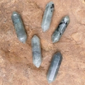 Set of five natural labradorite double-pointed hexagonal crystal columns on rock background - Labradorite
