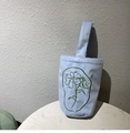 Vue détaillée du sac en toile à rayures bleu clair avec broderie florale verte sur marbre - Bleu clair