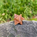 Handcrafted goldstone Merkaba energy star with shimmering particles on grey rock - Gold Sand Stone (Synthetic)