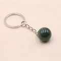 Dark green gemstone sphere keychain with silver metal ring on beige fabric background - India Agate