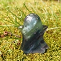 Carved natural fluorite ghost figurine with green and purple stripes on mossy ground - Colorful Fluorite