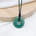 Natural green jade donut pendant necklace with black hand-woven cord on wood tray - Green Aventurine