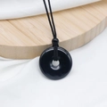Black obsidian donut pendant with adjustable braided cord on a zen wooden display - Obsidian
