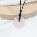 Pink quartz donut pendant necklace with black braided cord on a wooden display stand - Rose Quartz