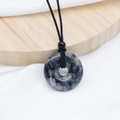 Natural labradorite donut pendant necklace with black braided cord on a white fabric base - Larvikite