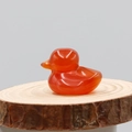 Translucent orange carnelian agate carved duck figurine on a rustic wooden slice - Red Agate