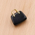 Colgante de mini bolso negro con asa de metal dorado sobre fondo de madera clara - Obsidiana