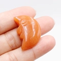 Hand holding an orange moon face carving made from natural orange aventurine stone - Red Aventurine