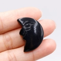 Polished black crystal crescent moon face carving held between fingertips - Obsidian