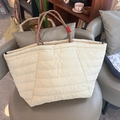 Detailansicht der cremefarbenen Stepptasche mit roten geflochtenen Henkeln auf einem Stuhl - Groß / Beigegrau