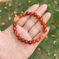 Hand holding red natural stone beaded bracelet with orange skull charms and silver spacers - Red Agate