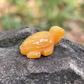 Hand-carved orange agate turtle figurine shown on a natural rock background - Topaz