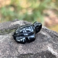 Polished black obsidian turtle carving featuring detailed shell texture on grey rock - Obsidian