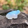 Translucent opalite sea turtle figurine with detailed shell carving on gray rock - Opal (Synthetic)