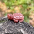 Carved reddish-brown natural crystal turtle figurine placed on a natural grey rock - Purple Aventurine