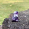 Mini hand-carved natural amethyst rabbit figurine on a dark stone outdoor background - Amethyst