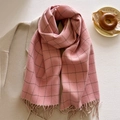 Detailed view of pink plaid scarf with long fringes laid on a warm beige coat - Pink