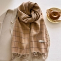 Plaid tassel scarf in camel and khaki colors draped over a stylish beige winter coat - Tan
