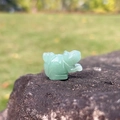 Mini hand-carved green aventurine frog figurine on a natural rock surface - Green Aventurine