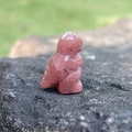 Mini dinosaur figurine carved from natural strawberry quartz gemstone on a dark rock - Purple Aventurine