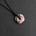 Ciondolo a ciambella in rodonite rosa con cordino nero intrecciato su sfondo scuro - Rodocrosite