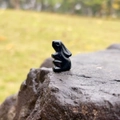 Polished black obsidian stone rabbit figurine placed on a natural rock surface - Obsidian