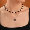 Detail van een gelaagde ketting met zwart-witte kralen en een vlinderhanger aan de ketting - Zwart-Witte Kralenketting Vlinder (24284-colour)