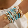 Detalle de pulseras de estilo bohemio con conchas y estrellas de mar lucidas en la muñeca - Multicolor (27269)