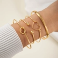 Dettaglio di un set di 5 bracciali dorati con ciondolo a cuore su manica in maglia bianca - Set da 5 pezzi con decorazione a cuore e nodo (29260-G) / Oro
