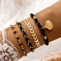 Detail of layered bohemian bracelets featuring gold shells and black beads on a model wrist - Black