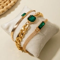 Detailed view of three gold-tone chain bracelets with emerald green gems on a pillow - 3-Piece Cuban Snake Chain Emerald Style (31292-bra-G)