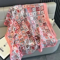 Detailed view of large silk scarf with coral and grey geometric prints on a leather sofa - Pink