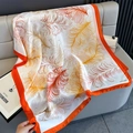 Detail of a botanical silk scarf with orange feather prints and vibrant border on a leather sofa - White