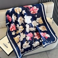 Detail eines Seidenschals mit Blumendruck und Schriftzug auf einem beigen Ledersofa - Blau