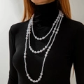 Dettaglio di una collana di perle a tre strati su un top nero a collo alto - Collana lunga di perle artificiali bianche a doppio strato (27453-white)