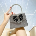 Silver rhinestone evening bag with black diamond bow and round handle held by hand - Black