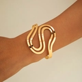 Close-up of a wavy S-shaped golden metal cuff bracelet on model's wrist with mirror finish - Golden S-Shaped Wave Style (29720-2-G)