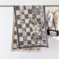 Close-up of checkered knit scarf with flower pattern and fringe detail on hanger - Gray