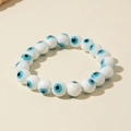 Detailed view of white ceramic beads with blue evil eye motifs on elastic bracelet - Faceted White (30529-bra-white-5)