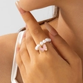 Gros plan d'une bague en perles avec pendentif papillon rose sur la main - Bague Élastique en Perles Blanches Papillon Rose (30573-ring-white-EP)