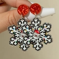 Gros plan de boucles d'oreilles flocon en acrylique avec motif Père Noël et clous rouges - Flocon de Neige Père Noël