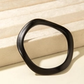 Macro detail of a minimalist black wavy acrylic bangle on a soft beige jewelry display - Irregular Wave Style (31202) / Matte Black