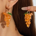 Close-up of dangling orange grape cluster earrings with green leaf detail on a model - Orange